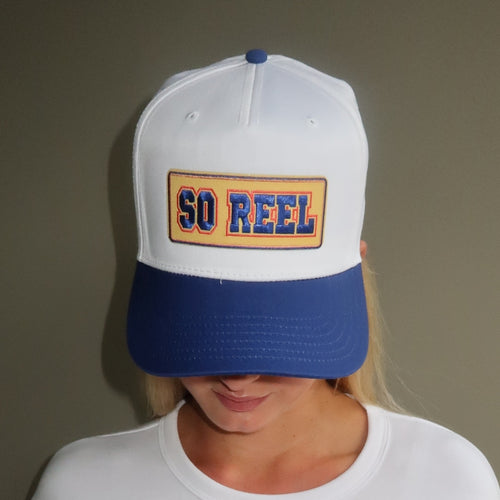 Person wearing a white and blue cap with 'SO REEL' text on a plain background